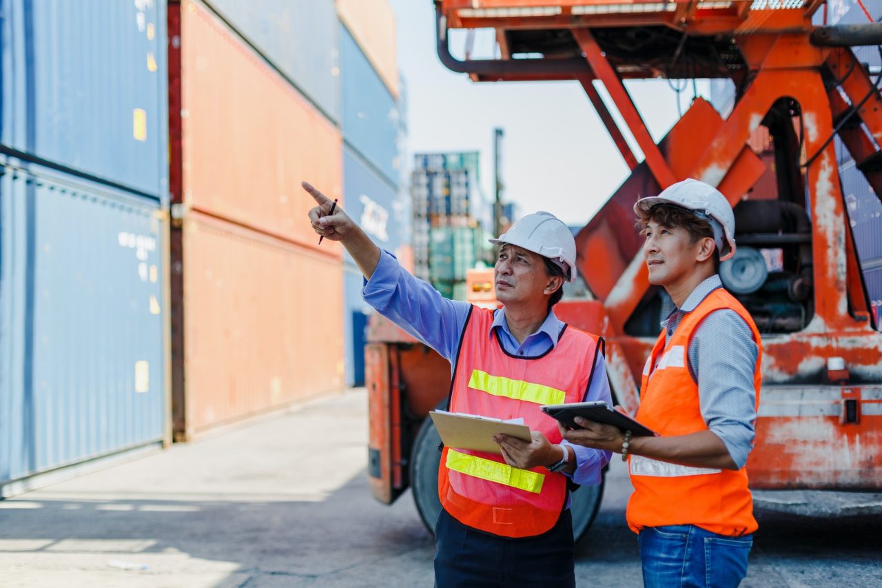 asian foreman and engineer holding clipboard control loading containers box in cargo .jpg
