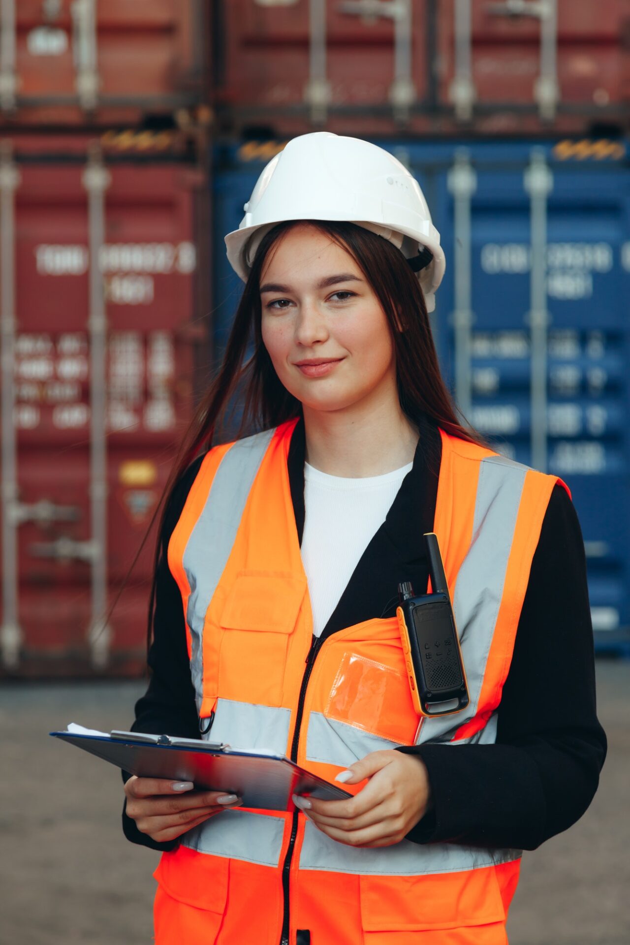 portrait of engineer woman with walkie talkie in white helmet and vest in container terminal e1701604903128.jpg